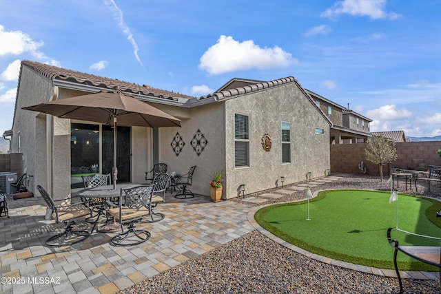 rear view of house featuring a tile roof, a fenced backyard, a patio, and stucco siding