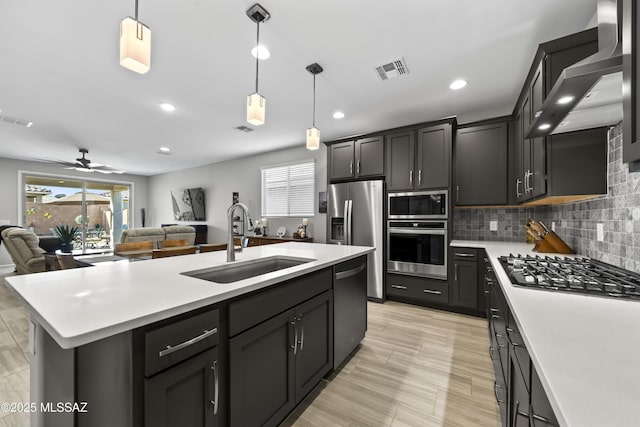 kitchen featuring a sink, visible vents, open floor plan, appliances with stainless steel finishes, and wall chimney exhaust hood