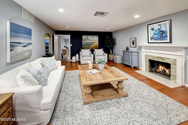 living room featuring a fireplace with flush hearth, wood finished floors, visible vents, and recessed lighting