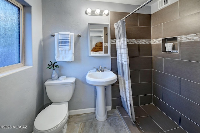 bathroom featuring visible vents, a tile shower, toilet, and baseboards