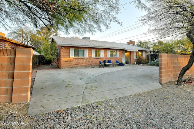 back of property with a chimney, fence, concrete driveway, and brick siding