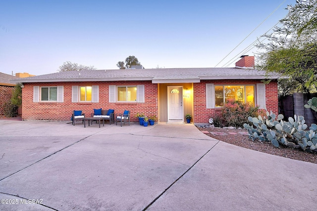 ranch-style house featuring brick siding, a chimney, and roof with shingles