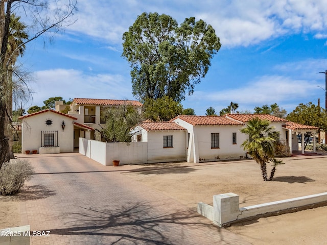 mediterranean / spanish house featuring decorative driveway, a tile roof, stucco siding, a gate, and fence