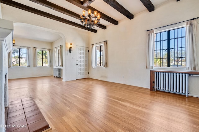 unfurnished living room with a chandelier, arched walkways, wood finished floors, and radiator