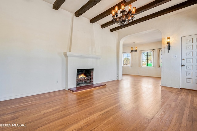 unfurnished living room with arched walkways, a notable chandelier, a large fireplace, wood finished floors, and beamed ceiling