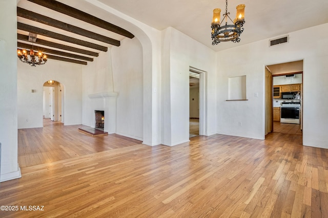 unfurnished living room featuring a warm lit fireplace, visible vents, arched walkways, an inviting chandelier, and light wood-style floors