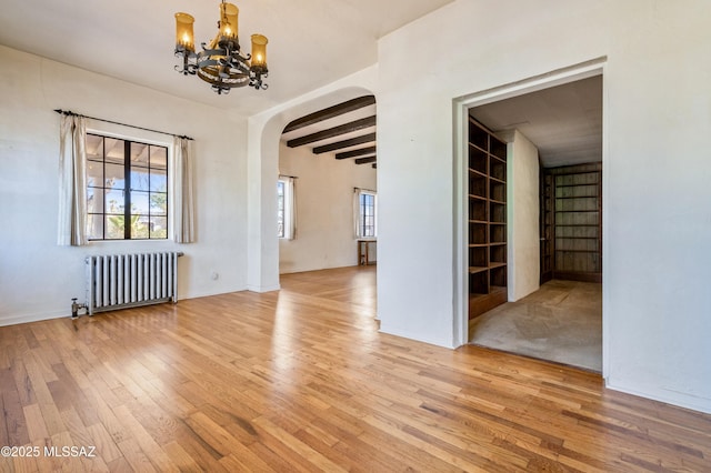 empty room with plenty of natural light, radiator heating unit, arched walkways, and wood finished floors