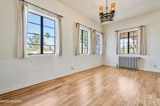 spare room featuring a chandelier, radiator, and wood finished floors