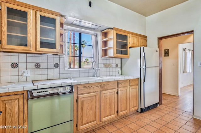 kitchen with dishwashing machine, a sink, freestanding refrigerator, decorative backsplash, and glass insert cabinets