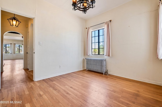 unfurnished room featuring arched walkways, a chandelier, baseboards, radiator, and light wood finished floors