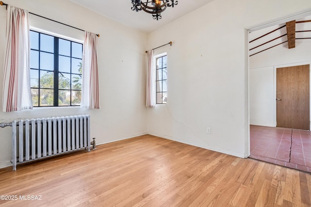 empty room with radiator, an inviting chandelier, wood finished floors, and beamed ceiling