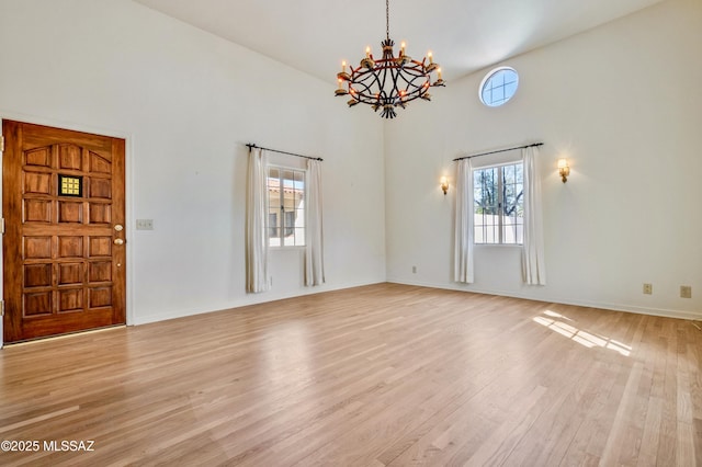 unfurnished living room featuring light wood-style flooring, a high ceiling, a chandelier, and baseboards