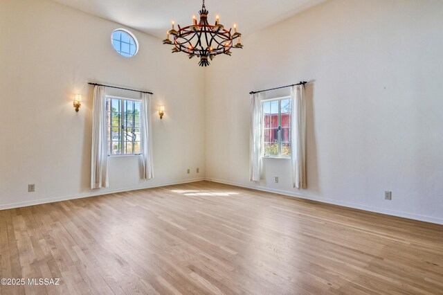 empty room with a wealth of natural light, baseboards, light wood finished floors, and an inviting chandelier