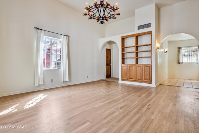 unfurnished room featuring light wood finished floors, visible vents, arched walkways, and a notable chandelier