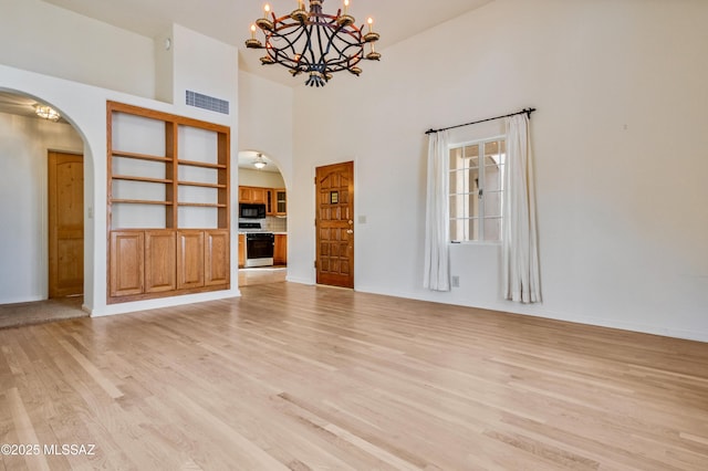 unfurnished living room with arched walkways, a chandelier, a towering ceiling, visible vents, and light wood finished floors