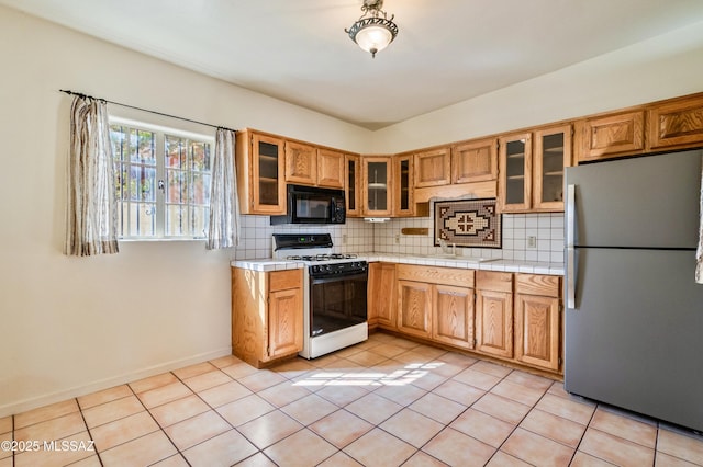 kitchen featuring gas range, black microwave, tasteful backsplash, and freestanding refrigerator