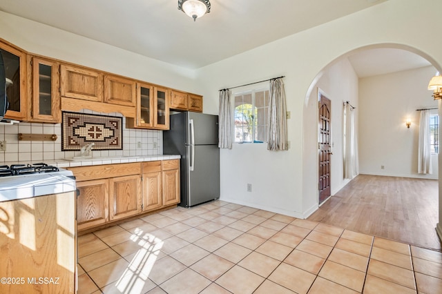 kitchen featuring arched walkways, decorative backsplash, freestanding refrigerator, gas stove, and light tile patterned flooring