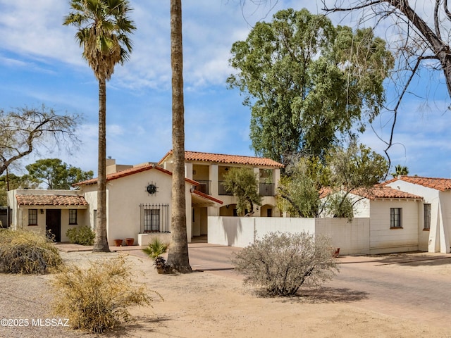 mediterranean / spanish house with a tile roof, fence, and stucco siding