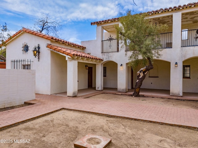 view of front of house with a patio, a balcony, fence, a tiled roof, and stucco siding