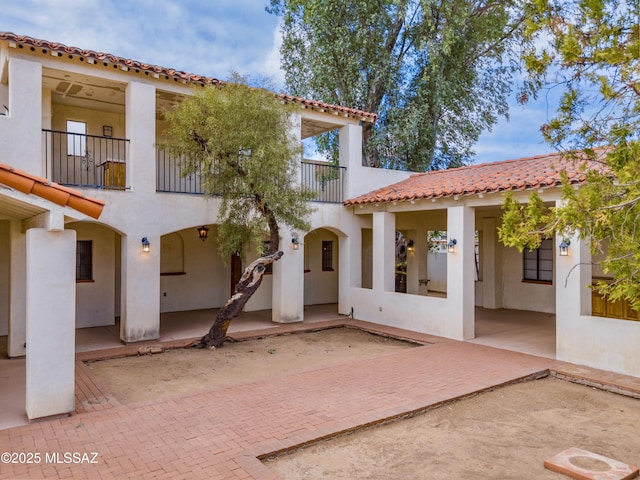 rear view of property with a patio area, a tile roof, a balcony, and stucco siding