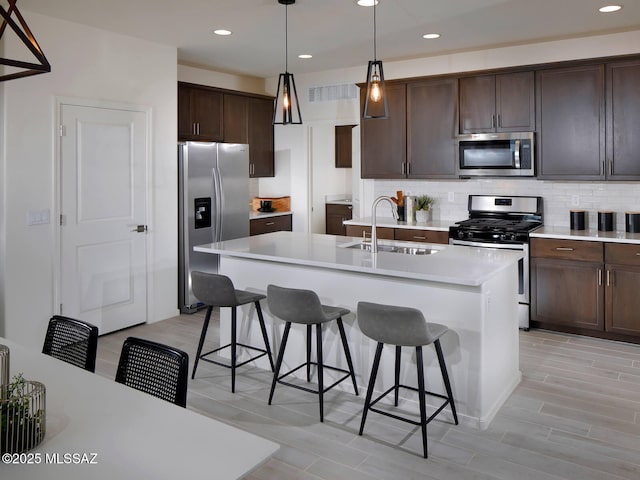 kitchen featuring a breakfast bar area, a sink, stainless steel appliances, dark brown cabinets, and tasteful backsplash