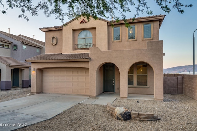 mediterranean / spanish-style house featuring concrete driveway, a tiled roof, an attached garage, fence, and stucco siding