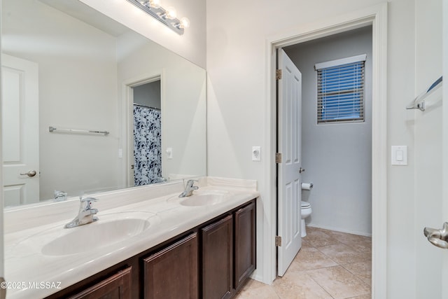 full bathroom featuring toilet, double vanity, a sink, and tile patterned floors