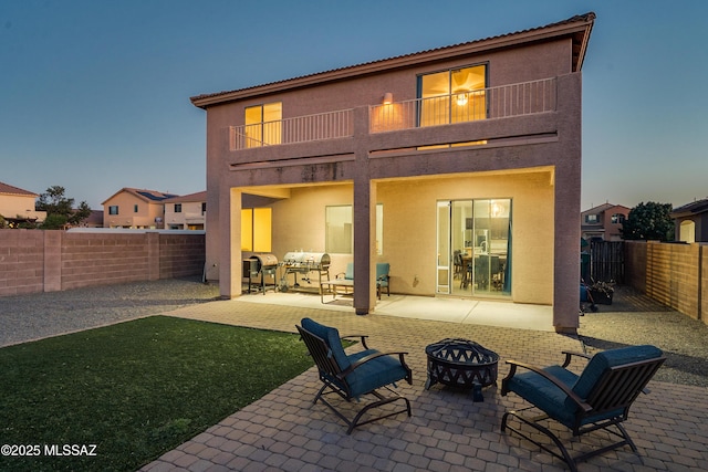 back of property with an outdoor fire pit, a patio, a balcony, a fenced backyard, and stucco siding