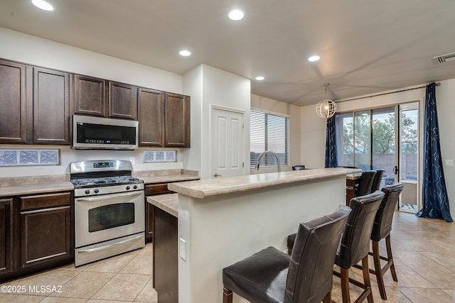 kitchen featuring a breakfast bar area, stainless steel appliances, dark brown cabinets, light countertops, and recessed lighting