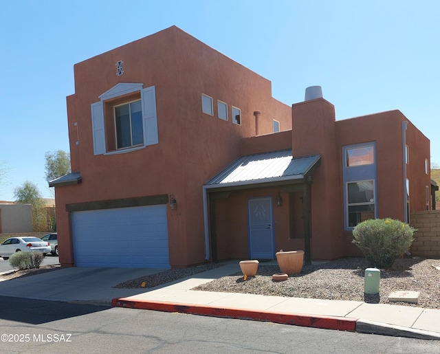 pueblo-style house with stucco siding, an attached garage, driveway, and metal roof