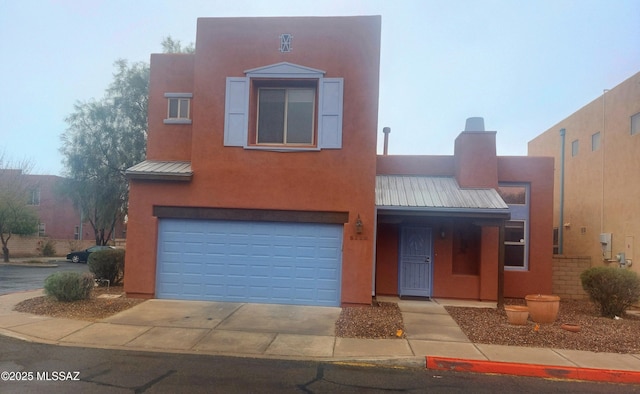 pueblo revival-style home with metal roof, a garage, concrete driveway, and stucco siding