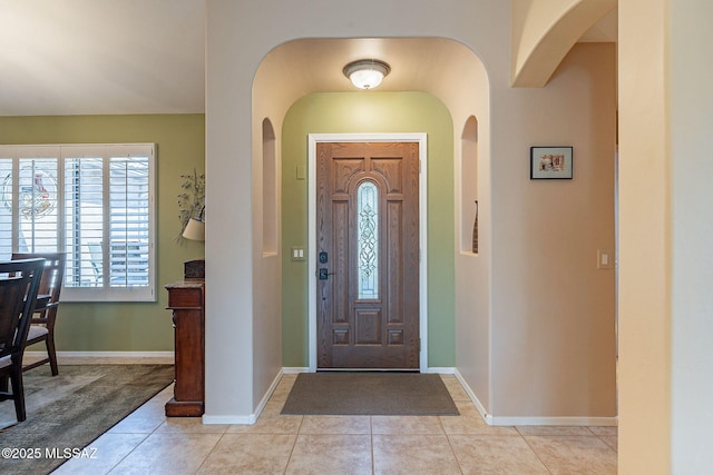 foyer entrance with baseboards, arched walkways, and light tile patterned flooring