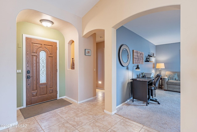 carpeted foyer with arched walkways, tile patterned flooring, and baseboards