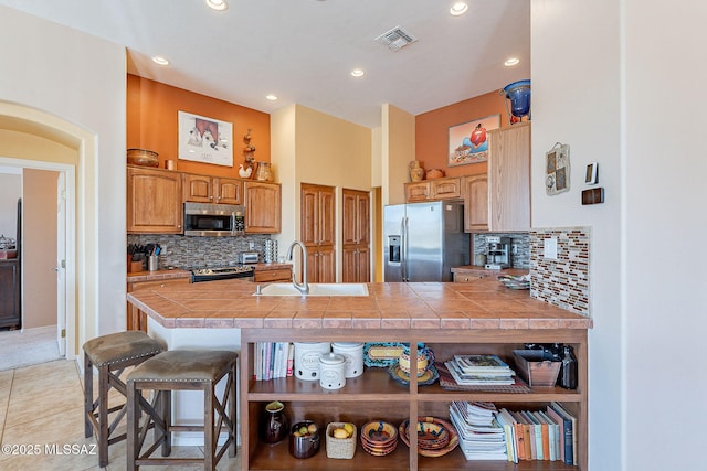 kitchen featuring visible vents, a breakfast bar area, a peninsula, stainless steel appliances, and a sink