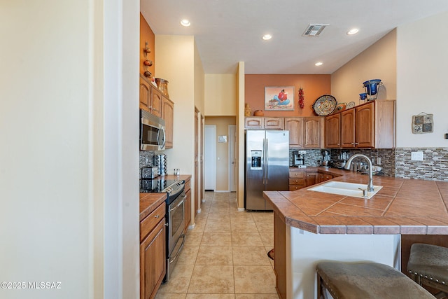 kitchen with visible vents, appliances with stainless steel finishes, a peninsula, a kitchen bar, and a sink