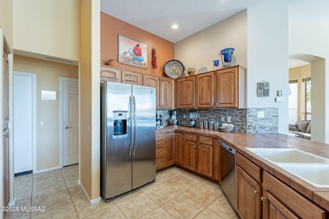 kitchen with stainless steel appliances, arched walkways, brown cabinets, and a high ceiling