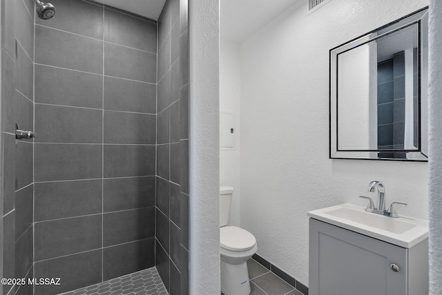 full bathroom featuring a textured wall, tile patterned flooring, toilet, vanity, and a tile shower