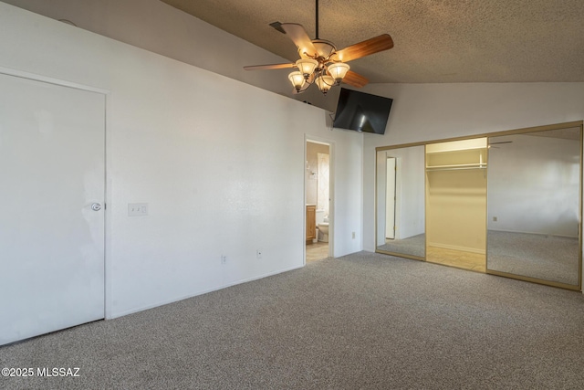 unfurnished bedroom with vaulted ceiling, carpet, a textured ceiling, connected bathroom, and a closet