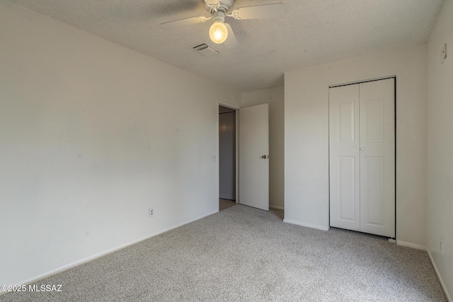 unfurnished bedroom with light colored carpet, a textured ceiling, ceiling fan, visible vents, and a closet