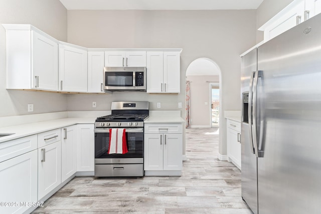 kitchen featuring light wood-type flooring, light countertops, appliances with stainless steel finishes, arched walkways, and white cabinets