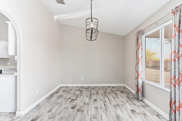 unfurnished dining area with light wood finished floors, visible vents, baseboards, arched walkways, and a notable chandelier