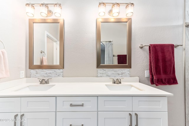 full bath featuring double vanity, a textured wall, and a sink