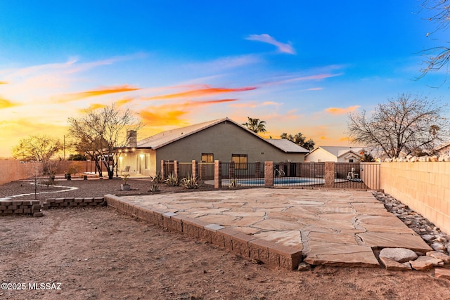 back of property at dusk with stucco siding, a fenced in pool, a fenced backyard, and a patio area