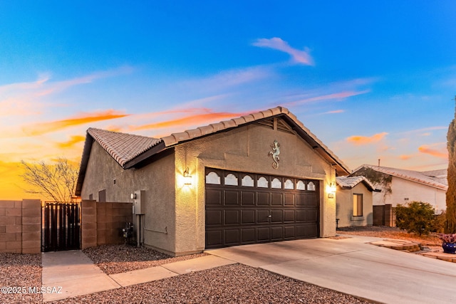 view of front of house featuring fence, a tile roof, stucco siding, driveway, and a gate