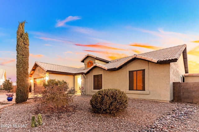 view of front of property with stucco siding, an attached garage, a tile roof, and fence