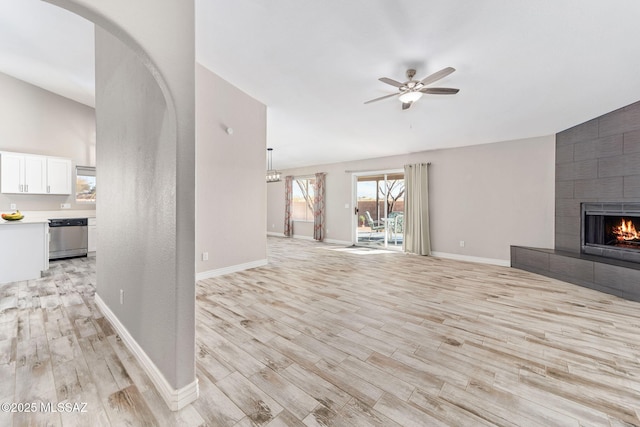 unfurnished living room with a ceiling fan, a tiled fireplace, arched walkways, light wood finished floors, and baseboards