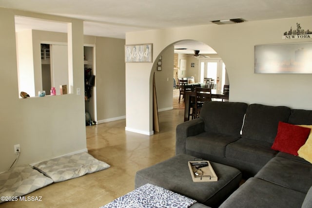 living area featuring arched walkways, ceiling fan, visible vents, and baseboards