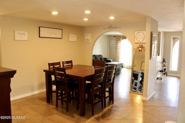 dining room featuring concrete flooring, baseboards, arched walkways, and recessed lighting