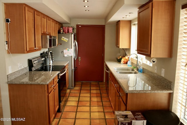 kitchen featuring brown cabinetry, light stone counters, appliances with stainless steel finishes, a sink, and recessed lighting