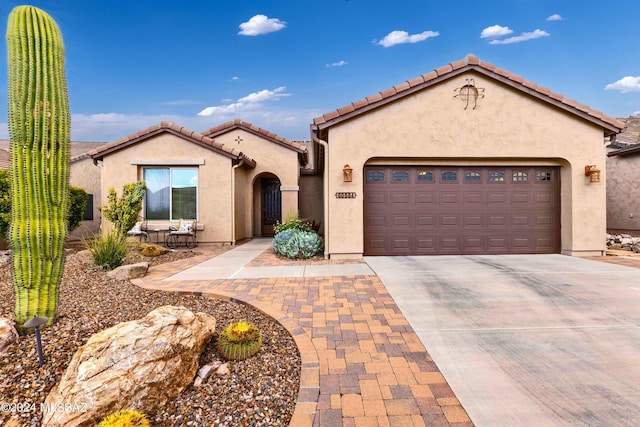 mediterranean / spanish-style home featuring a garage, a tile roof, driveway, and stucco siding